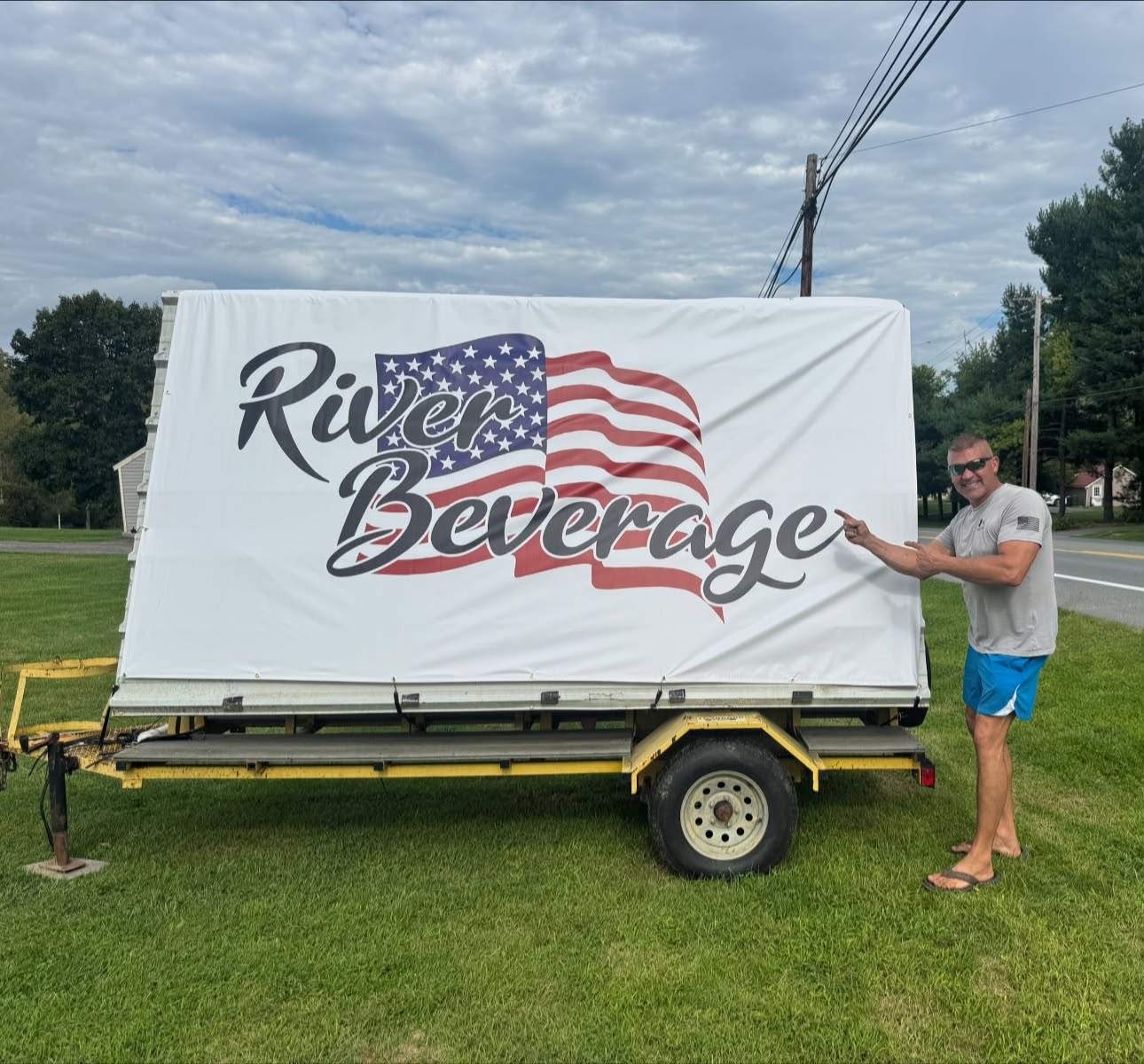 Owner John Vaughn pointing at the River Beverage sign on a trailer along Lincoln Highway